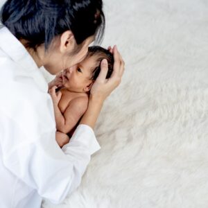 White shirt mother is kissing and holding newborn baby near fluffy bed with concept love and careful for baby